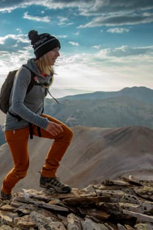 A man and a woman hiking up a rocky mountain trail with mountain ranges visible in the distance behind them.