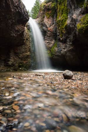 A tall waterfall starting at an opening in the ground and cascading into a deep hole below.