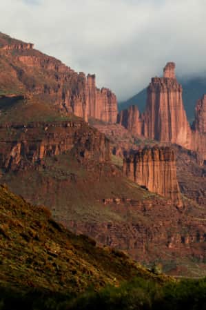 Tall red rock tower formations surrounded by mountains and clouds.