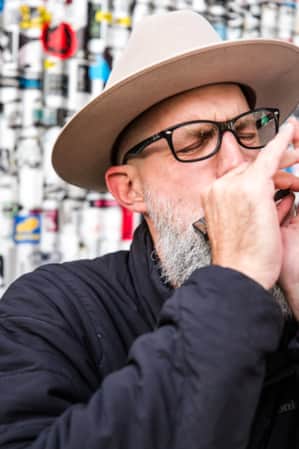 A man playing the harmonica in front of a metal wall covered in stickers.