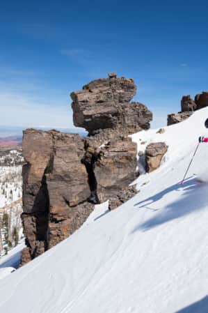 A skier making first tracks down a mountain, surrounded by scattered rocks and trees