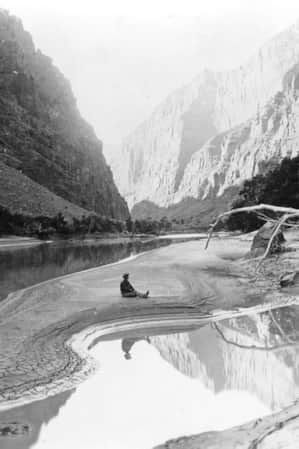 A man sitting at the base of a canyon surrounded by massive cliff faces.