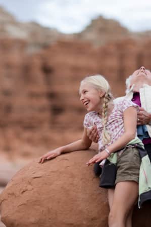 A woman and young girl leaning against a red rock, laughing.