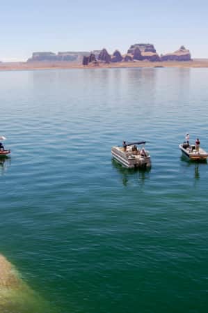 A still lake with rock formations in the background, and boats anchored along the shore.