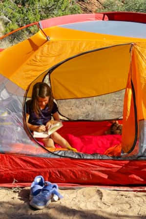 A young child inside a tent, writing in a book.