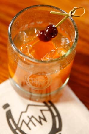 A small glass filled with a mixed drink, topped with a toothpick of cherries, resting on a white napkin.