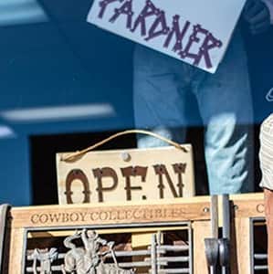 A man sitting on a bench wearing western clothing, in front of a store.