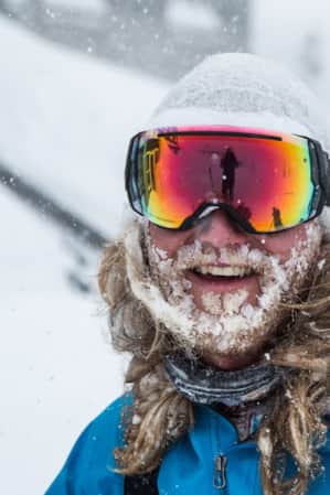 A man smiling while wearing winter clothing, with a long beard covered in snow.