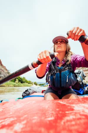 A woman rowing through a river, with tall cliffs rising on each side.