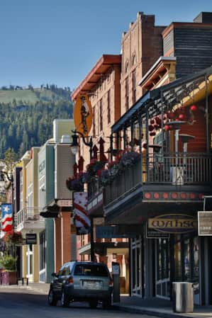 A historic downtown mountain town street, with green mountains and ski runs visible in the distance.