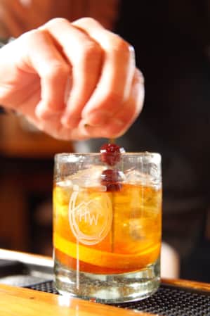 A bartender adding two cherries to the top of a drink.