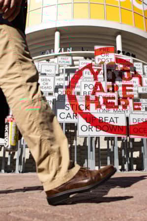 The legs of a person walking past an art installation made of street signs.