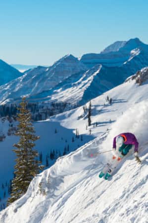 A skier making a turn down a snowy mountain, kicking up a spray of snow behind them.