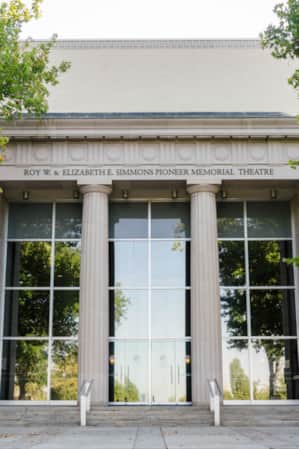 Two tall pillars flanking entrance doors to a building with the name 'Roy W. and Elizabeth E. Simmons Pioneer Memorial Theatre' displayed above.