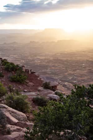 The side of a rocky mountain adjacent to a flat expanse of red rock in the desert.