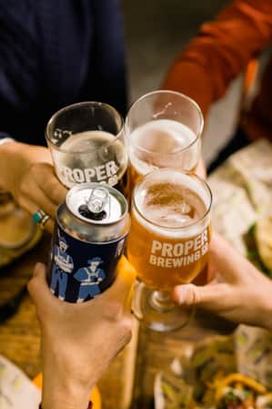 Aerial shot of four people clinking beer bottles and glasses.