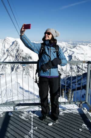 A woman wearing winter gear taking a selfie at the top of a mountain observatory.