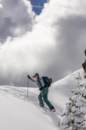 A woman snowshoeing through deep snow on the slope of a mountain.