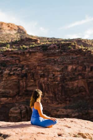A woman sitting and meditating while overlooking a red rock canyon.