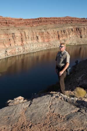 A park ranger standing on top of a large rock formation, looking out over a wide river.