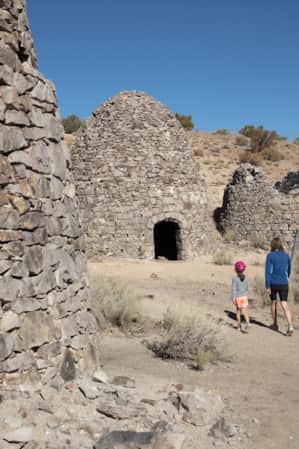 Woman and young girl walking on a trail surrounded by dome houses made of rocks.