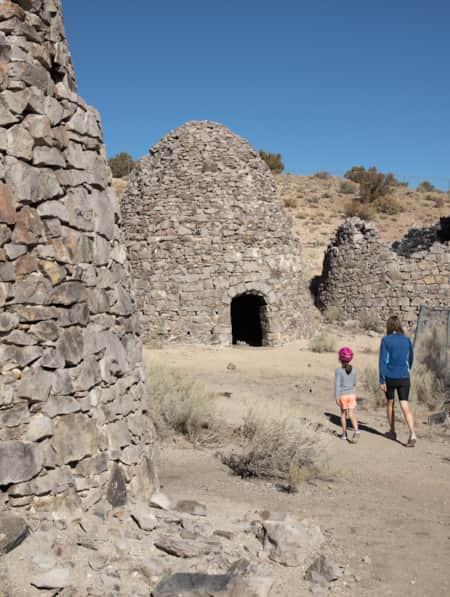 Woman and young girl walking on a trail surrounded by dome houses made of rocks.