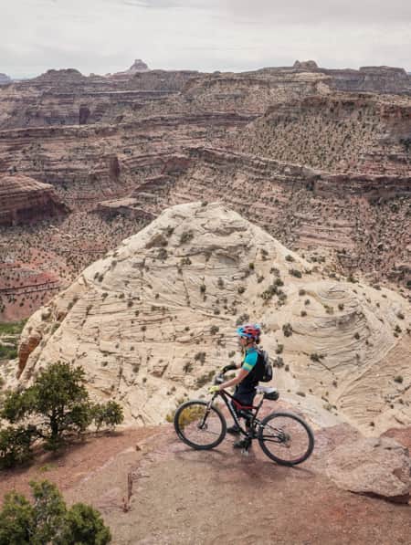 A cyclist at the top of a mountain, overlooking a landscape of large rocky mountains.