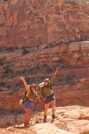Two female hikers smile and pose on a trail in Capitol Reef National Park.