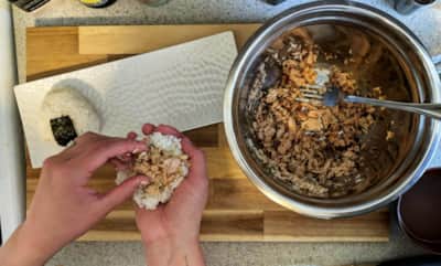 Someone stuffing a rice ball with salmon.