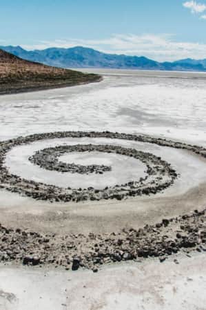 A spiral jetty extending into a salty lake during low tide, with a small brown hill visible in the distance.