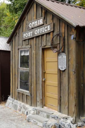 A man walking next to a wooden building with a sign reading 'Ophir Post Office.'