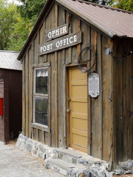 A man walking next to a wooden building with a sign reading 'Ophir Post Office.'