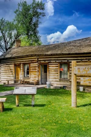 An old home made of wood logs, with a sign in the front yard reading 'Wilford Woodruff Home.'