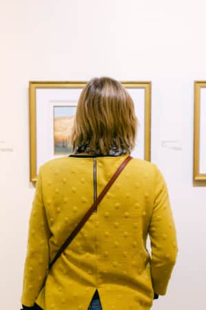View of a woman from behind, observing three art pieces hanging on a wall.