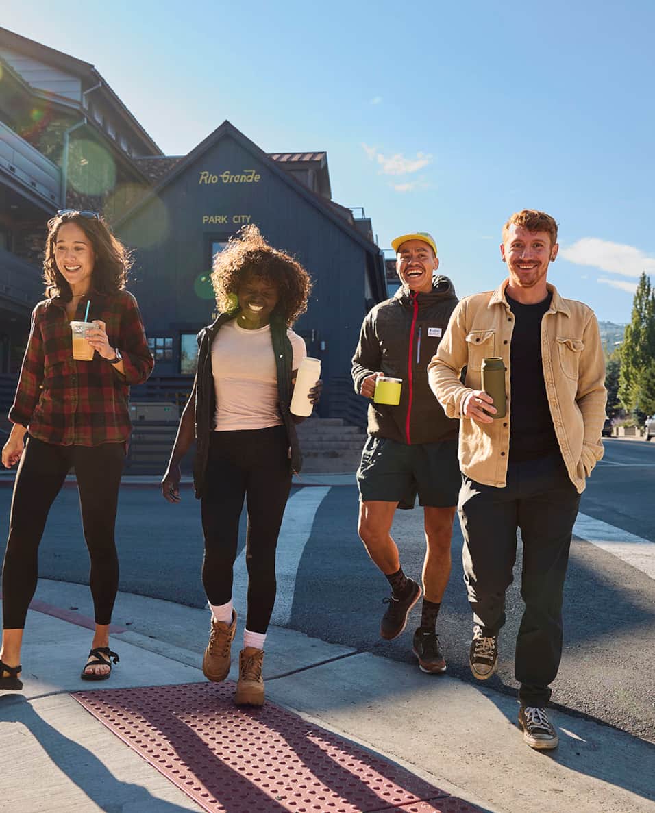 Group of four friends, holding coffees and walking through downtown Park City.