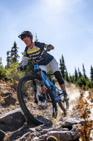A woman riding a mountain bike down a rocky dirt trail, leaving a trail of dust behind her.