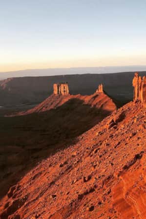 An expansive view of the desert with a large red rock monument glowing orange, illuminated by the sun.