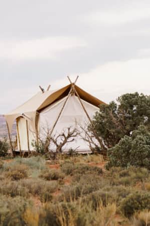 Canvas tent overlooking a desert landscape with red rock formations and green shrubbery.