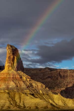Half of a rainbow arcs over a desert landscape with tall monument rock formations.