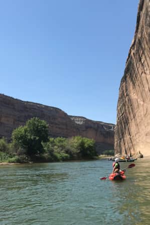 People rafting on the water, navigating between large cliffs.