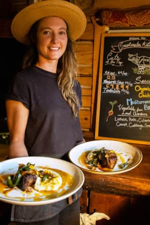 A woman holding two plates of elegantly arranged food in a restaurant with an all-wood interior.