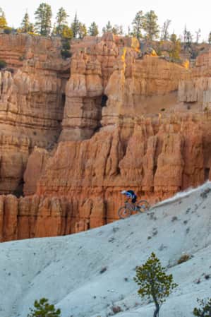 A person on a mountain bike riding down the ridge of a mountain, with hoodoos visible in the distance.