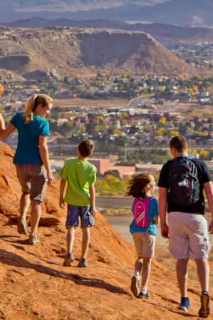 A family on a red rock formation overlooking the view of a city.
