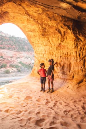 Two children standing in a sandy cave illuminated by sunlight.