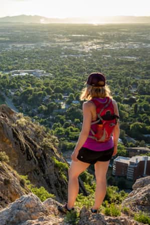 A woman standing on a mountain overlooking a valley with a city below, while a man on a lower rock level looks up at her.