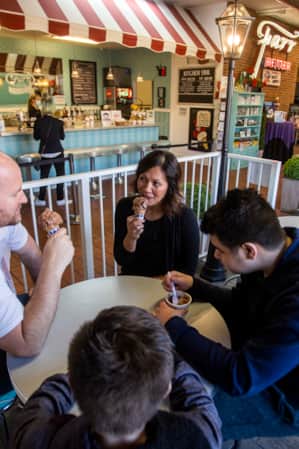 Two adults and two young children sitting at a table inside a creamery, each enjoying an ice cream cone.