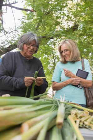 Two women talking while standing in front of a table with a long green plant on it.