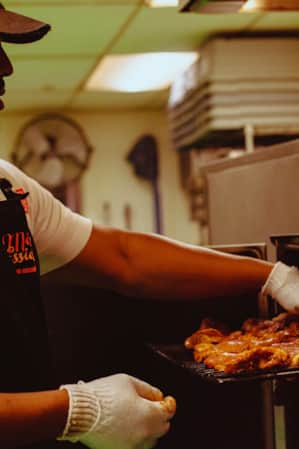A man checking on barbecued meat in an industrial air fryer.