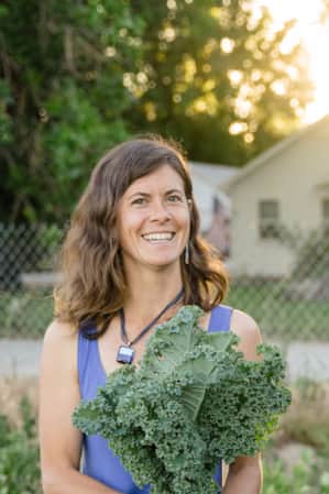 A man and a woman smiling, each holding a bundle of kale in an urban garden.