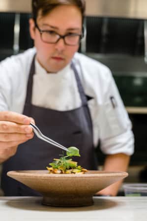 A chef adding the final garnish to a dish in a restaurant kitchen.